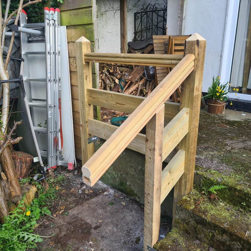 Newly built timber handrail fitted onto garden steps with a log store behind